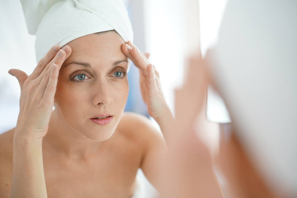 Woman looking in mirror with her hands on her forehead